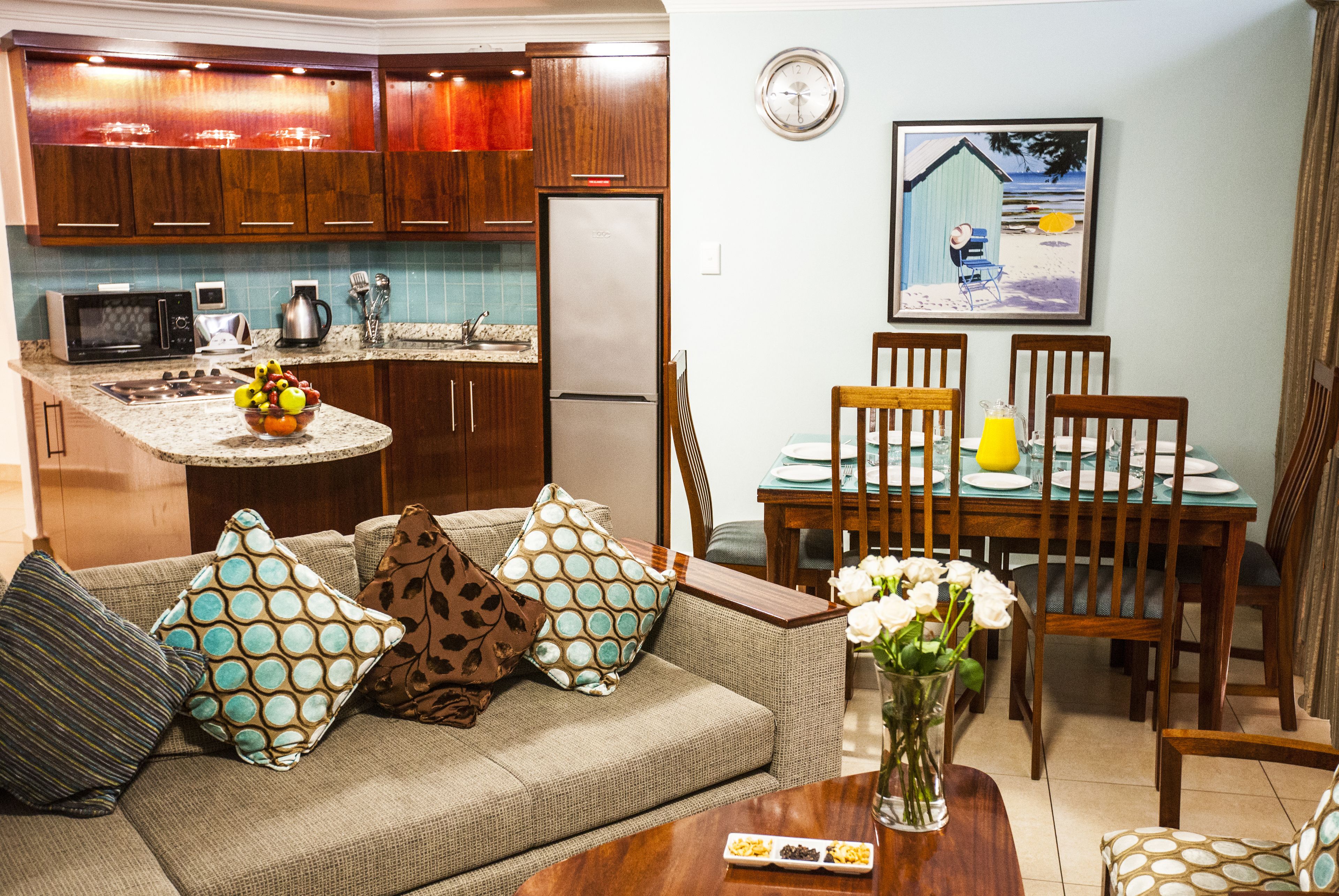 A compact kitchen with a refrigerator, microwave, and coffee maker. There is a dining area with a table, chairs, and a vase of flowers.