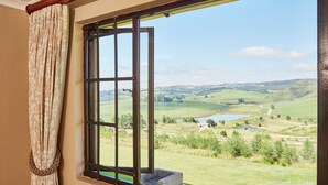 A room with a large window offering a view of a green landscape with hills and a lake. - First Group Midlands Saddle and Trout (Mooirivier)