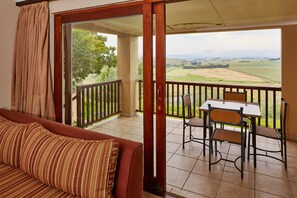 A balcony with a table and chairs, a sofa, and a view of a green landscape. - First Group Midlands Saddle and Trout (Mooirivier)