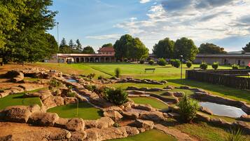 Stunning golf course with a well-manicured green and unique rock formations, set against a scenic backdrop of a building with a red roof and arched design.