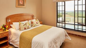 A neatly made bed with a wooden headboard, a bedside table with a lamp, and a view of a balcony with a railing.