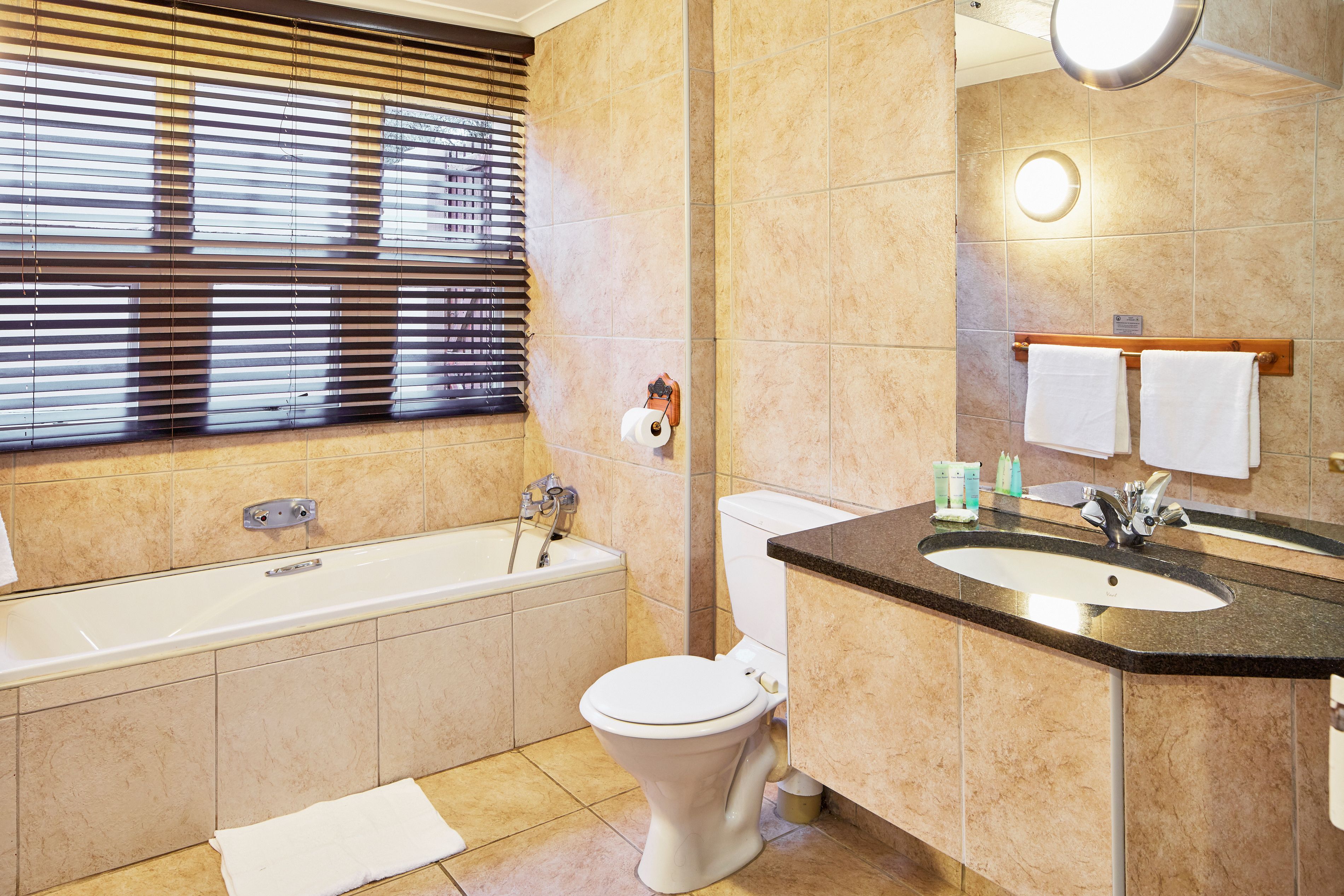 A bathroom with a bathtub, toilet, sink, and window with blinds.