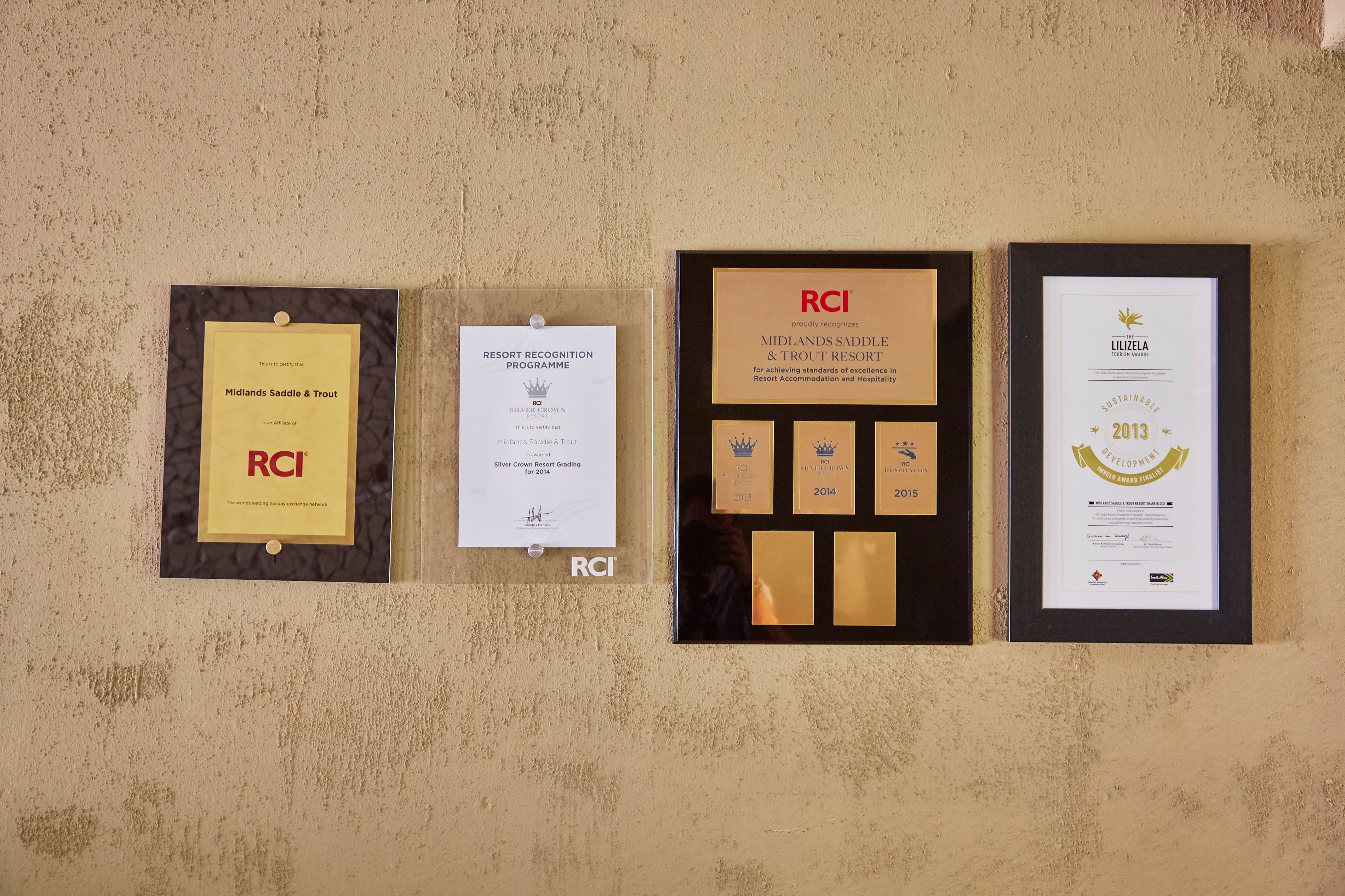 Premios y certificados enmarcados en una pared, incluyendo un premio 'Midlands Saddle & Trout', un certificado de 'Silver Crown Resort Grading' y un certificado 'Sostenible 2013'.