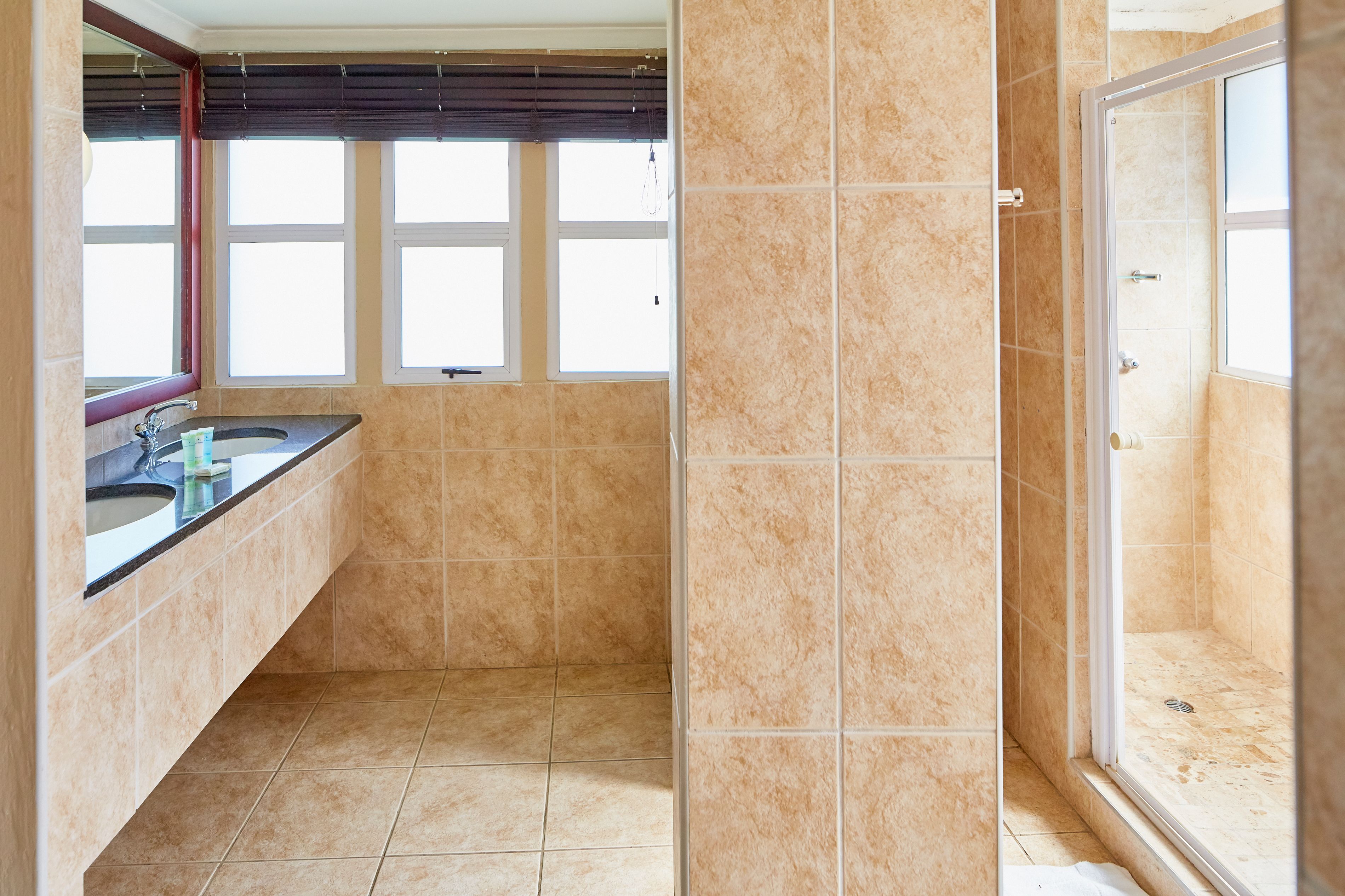 A bathroom with a large window, a shower, and a sink with a mirror.