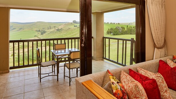 A balcony with a table and chairs, a sofa with patterned cushions, and a view of green hills. - First Group Midlands Saddle and Trout (Mooirivier)