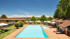 A rectangular swimming pool with a tiled deck, surrounded by lounge chairs and umbrellas, set against a backdrop of hills and a clear sky. - First Group Midlands Saddle and Trout (Mooirivier)