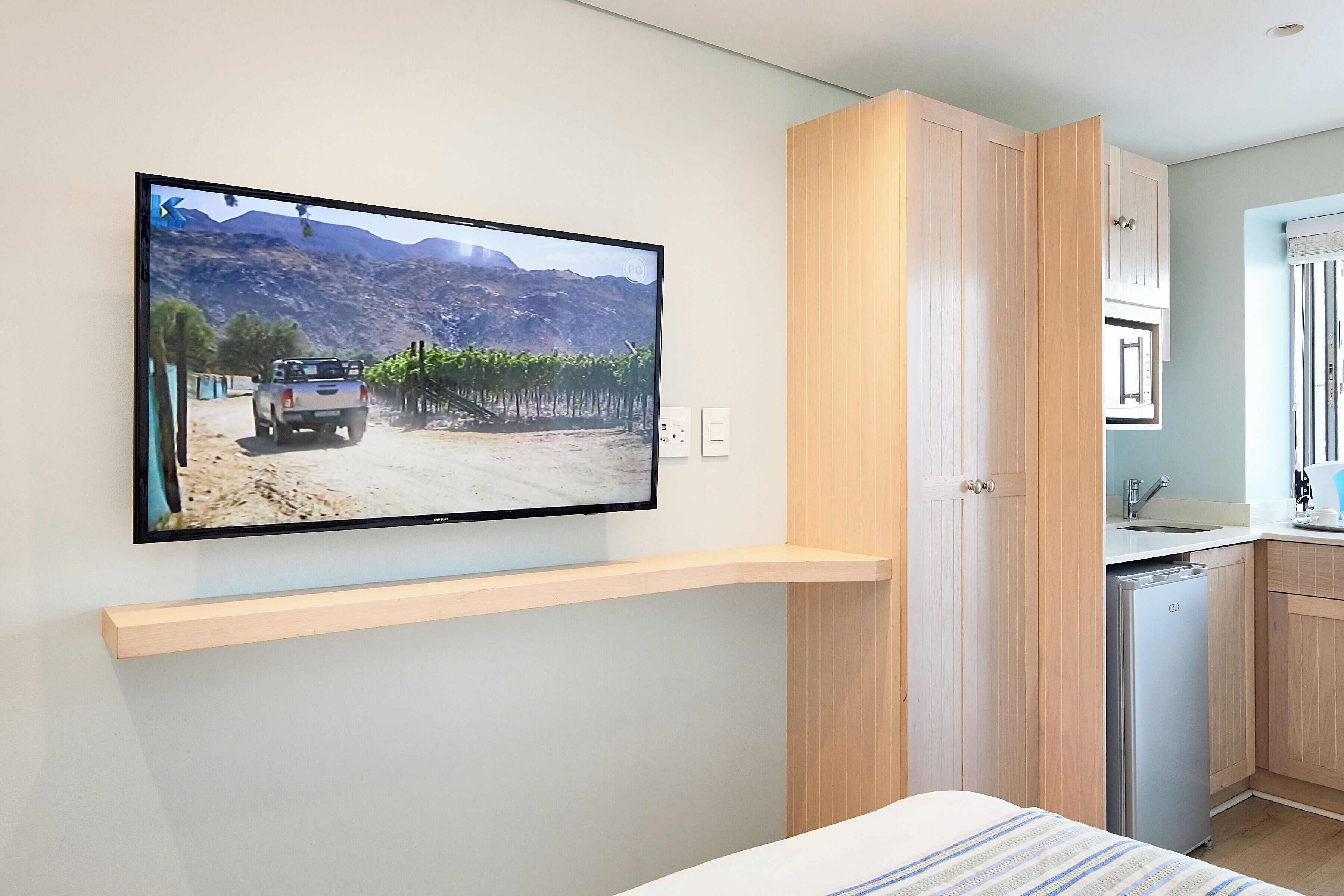 A modern kitchen with a built-in dishwasher, wooden cabinets, and a flat-screen TV mounted on the wall.