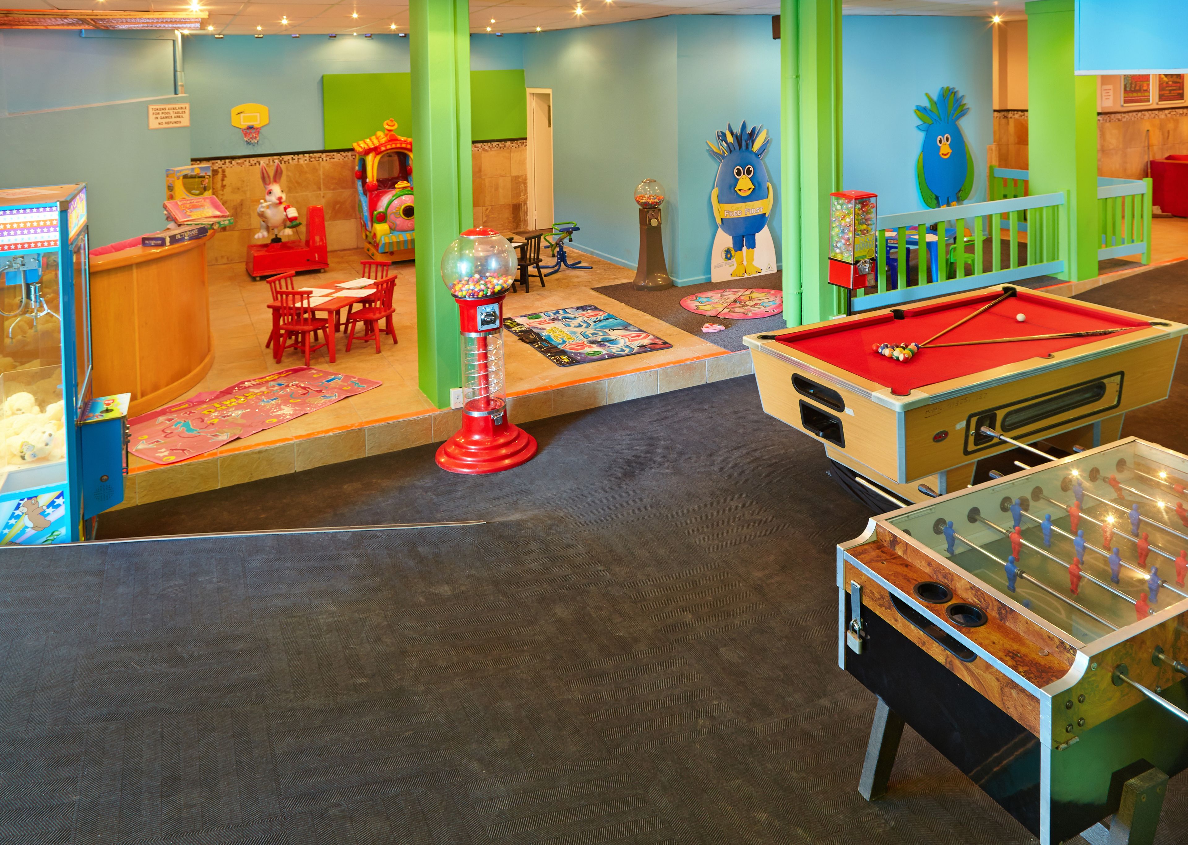 A brightly lit indoor play area with a foosball table, a ball pit, and a children's play station.