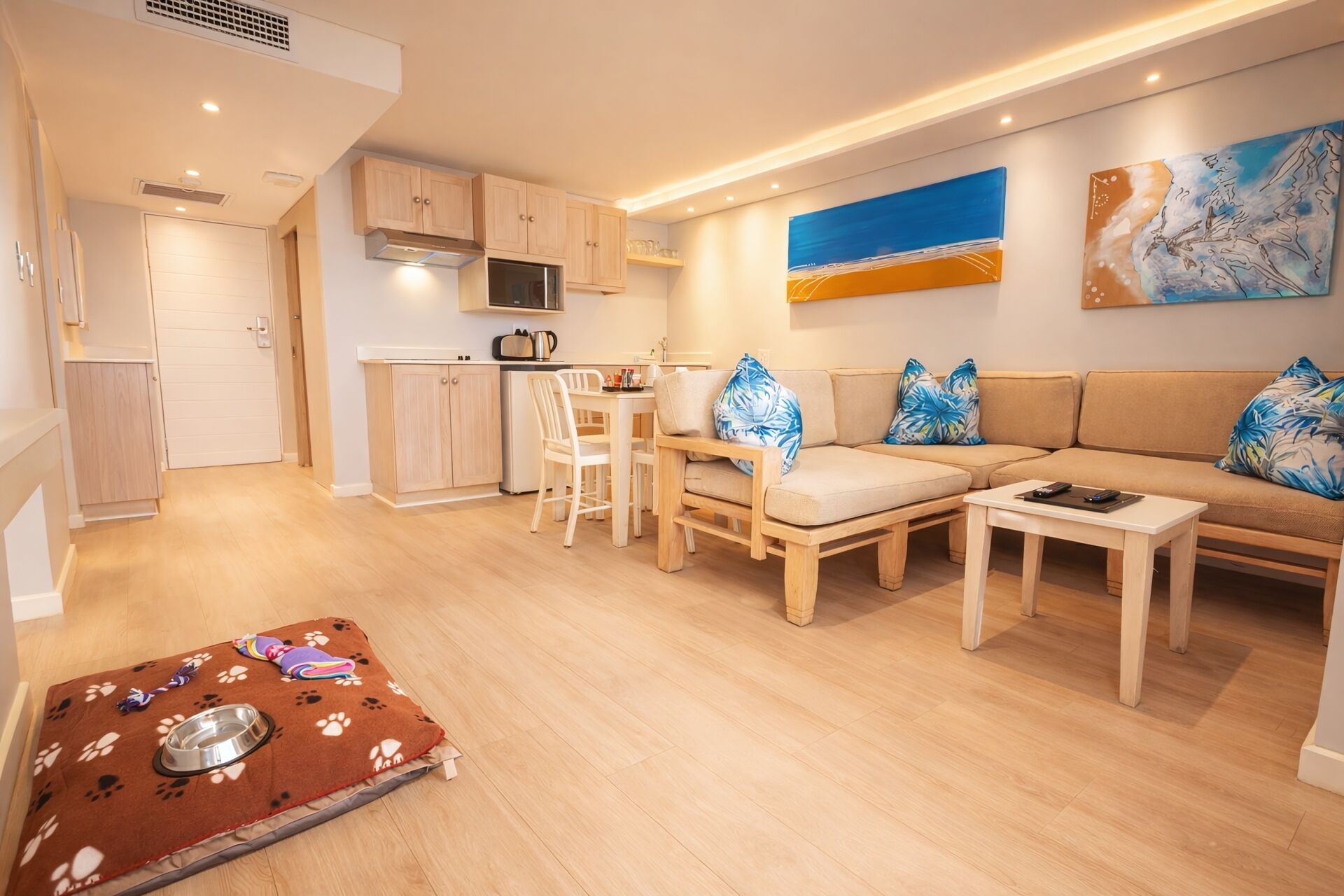 A modern living room with a sofa, coffee table, and dining table. There is a kitchen area with cabinets and a microwave.