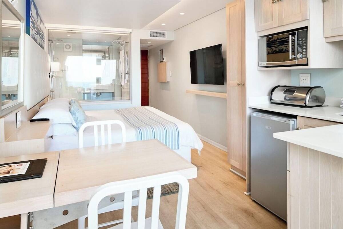 Habitación de hotel pequeña con cama, una mesita de comedor, kitchenette con microondas y televisor montado en la pared.
