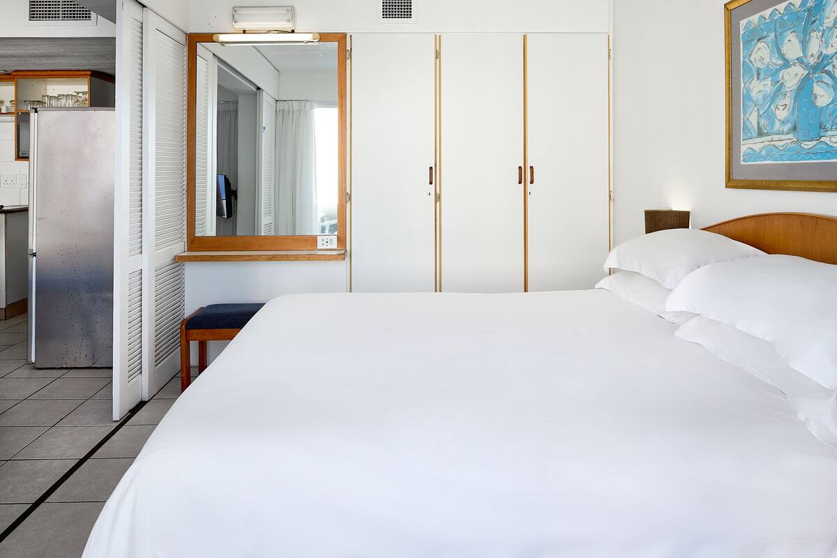 Habitación de hotel con una cama grande, un armario, un espejo y un cuadro en la pared.