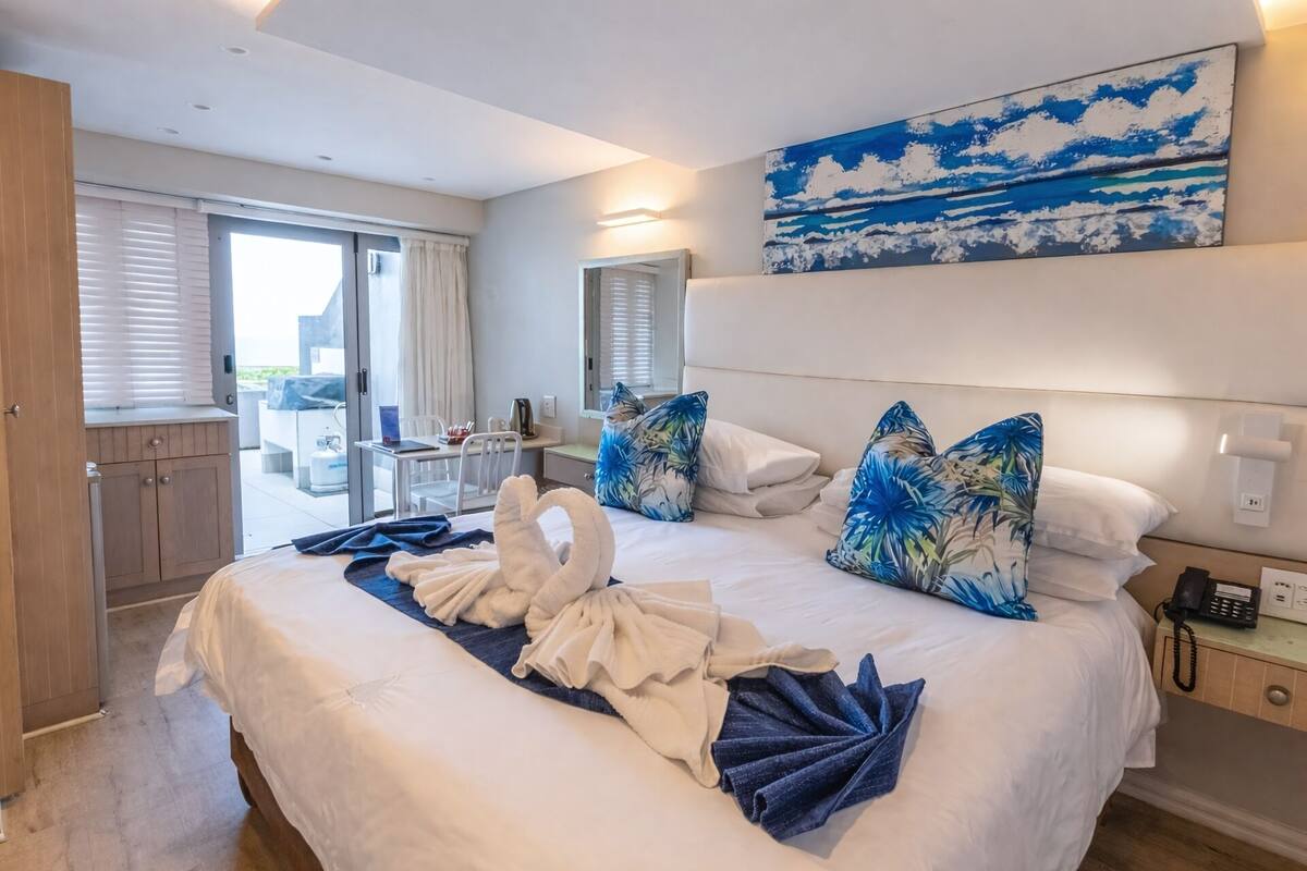 Habitación de hotel con cama, escritorio, una silla, vistas al exterior y un cuadro en la pared.