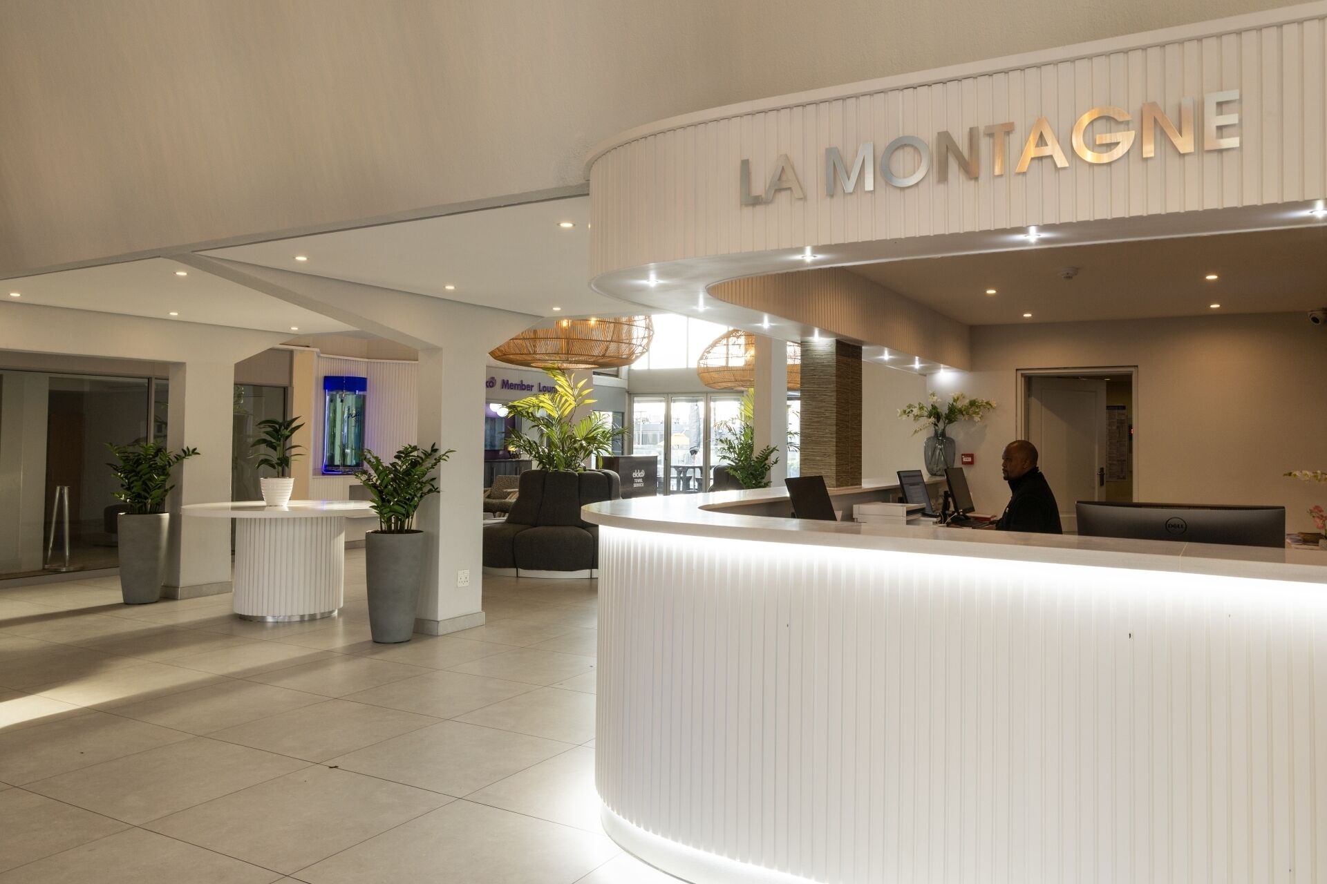 A modern hotel reception area with a curved reception desk, potted plants, and a sign reading "LA MONTAGNE".