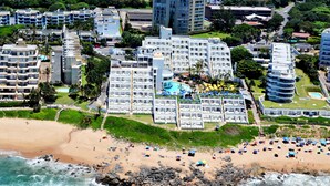 Um hotel na praia com várias varandas, uma piscina e uma área de praia com guarda-sóis.