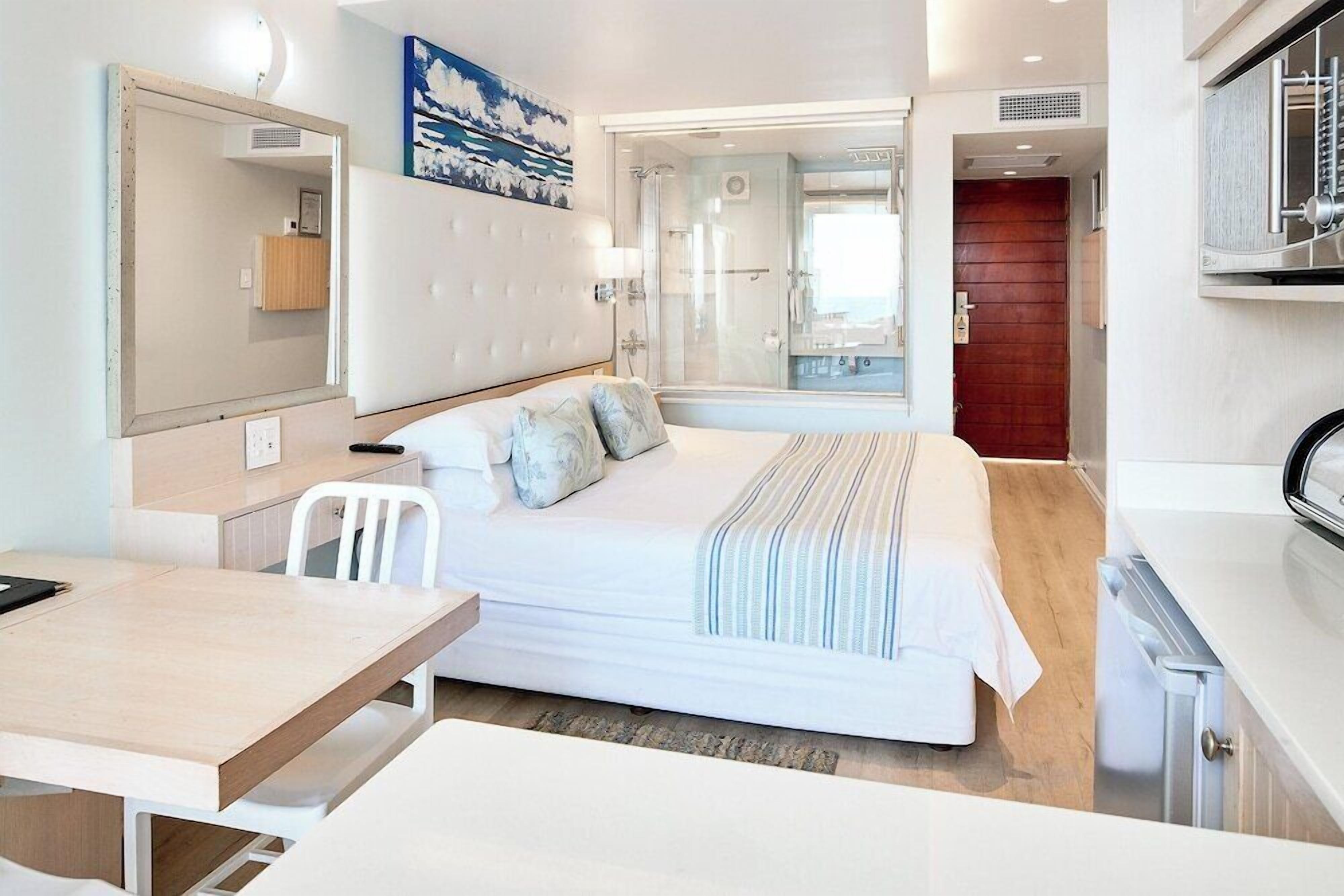 Ein modernes Hotelzimmer mit Bett, Schreibtisch, Stuhl, Spiegel und einer Dusche.