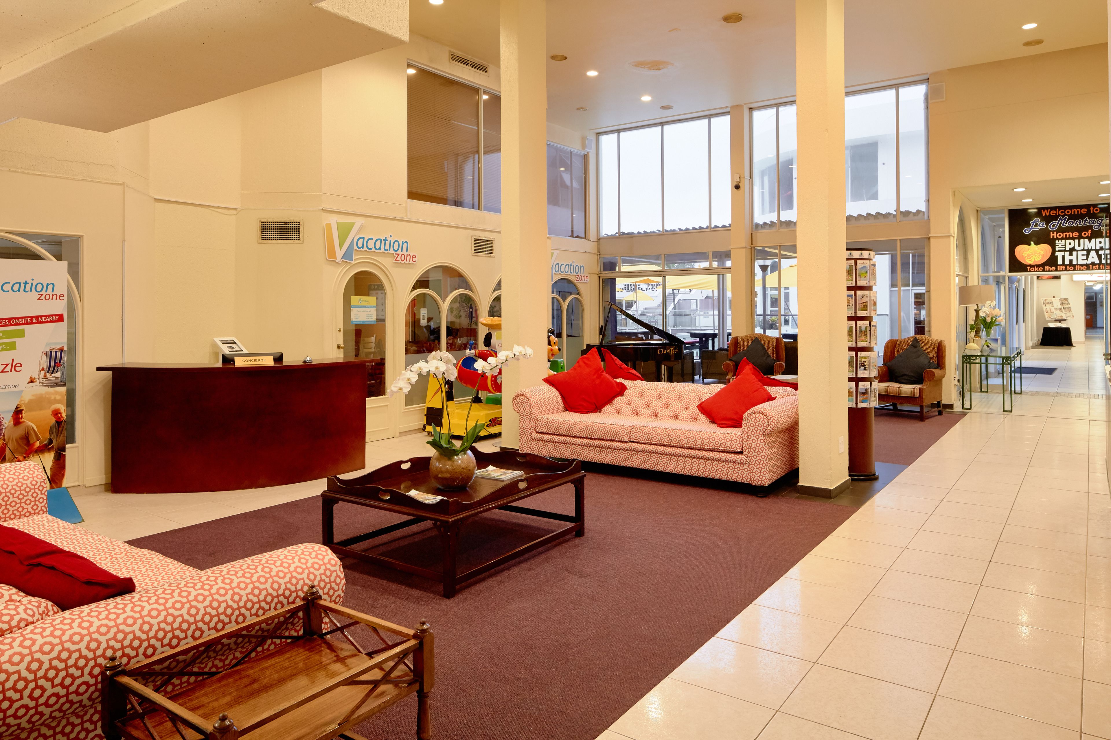 Um hall amplo com balcão de recepção, um piano, um sofá com almofadas vermelhas e uma mesa de centro.