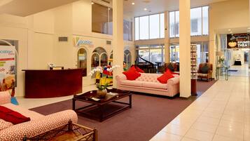 Um hall amplo com balcão de recepção, um piano, um sofá com almofadas vermelhas e uma mesa de centro.