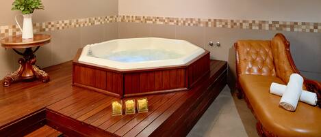 Un bagno con pavimento in legno, una grande vasca da bagno, una panca di legno e un piccolo tavolo con una pianta.