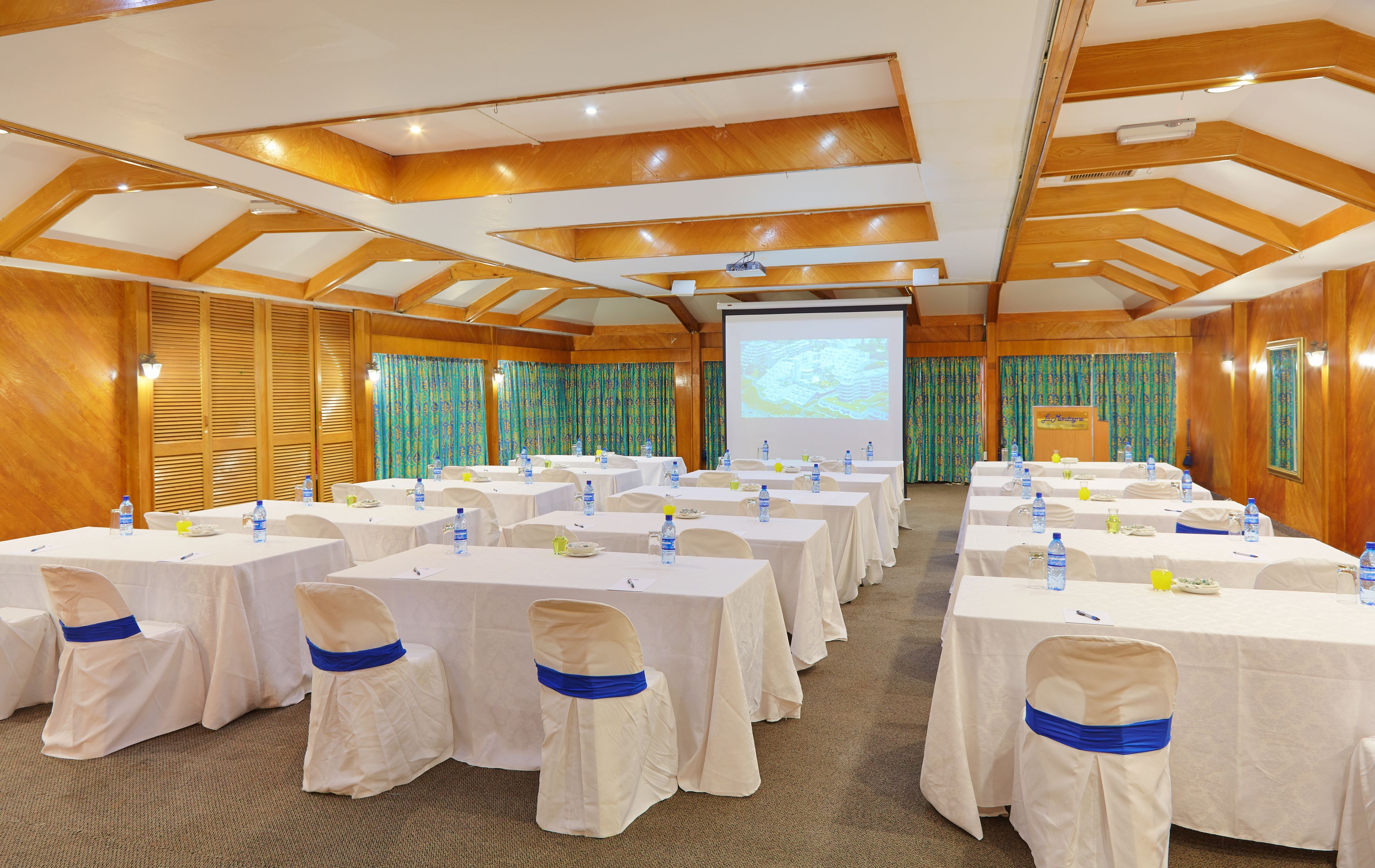 A conference room with multiple tables, chairs, and a projection screen.