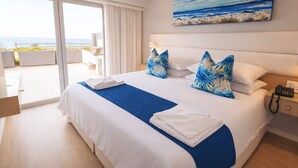 Quarto de hotel com uma cama grande, vista para o mar, uma pintura do mar e um telefone na mesa de cabeceira.