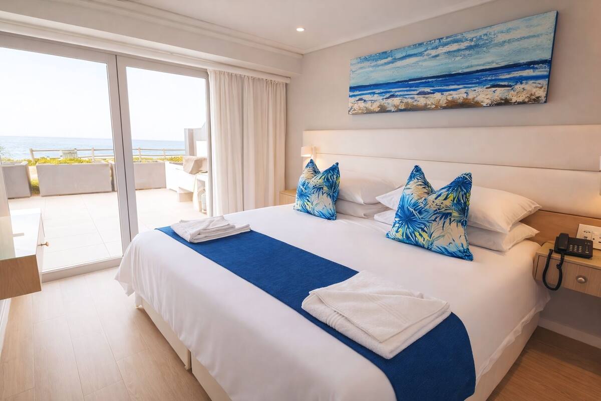 Habitación de hotel con una cama grande, vista al mar, un cuadro del mar y un teléfono en la mesita de noche.
