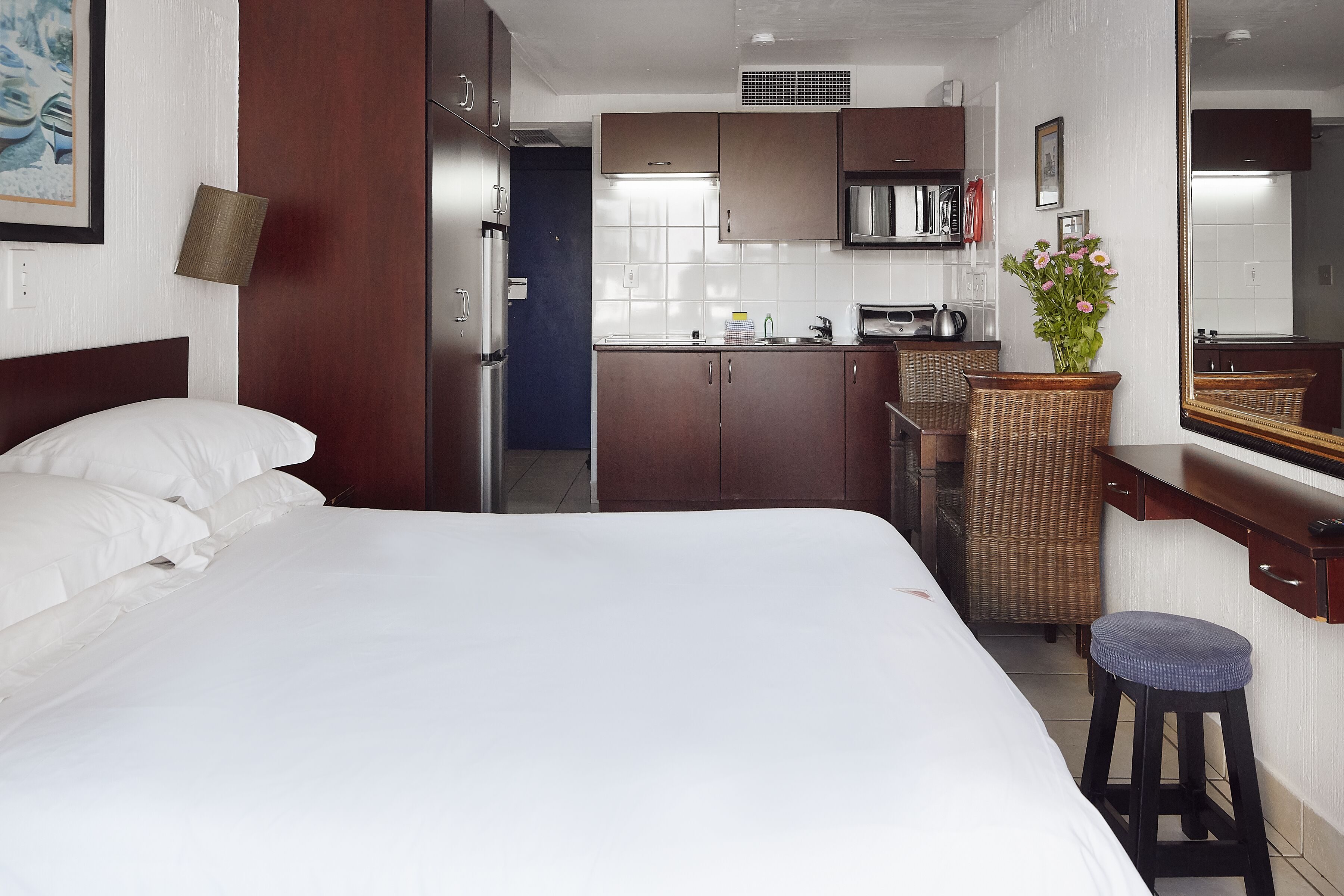 Una camera d'albergo con un letto, un angolo cottura, uno specchio e una poltrona in vimini.