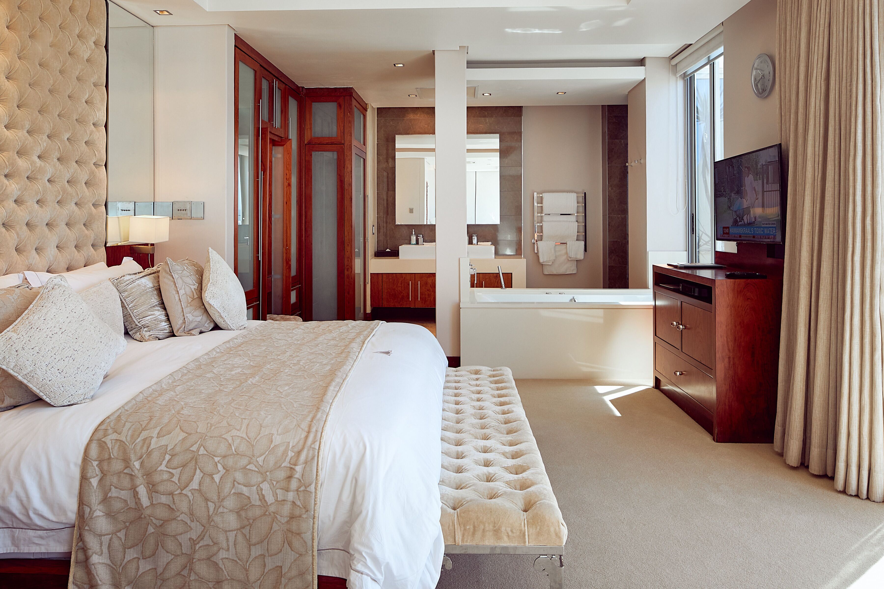 Habitación de hotel con una cama grande, zona de estar, tocador con espejo, bañera y televisión.