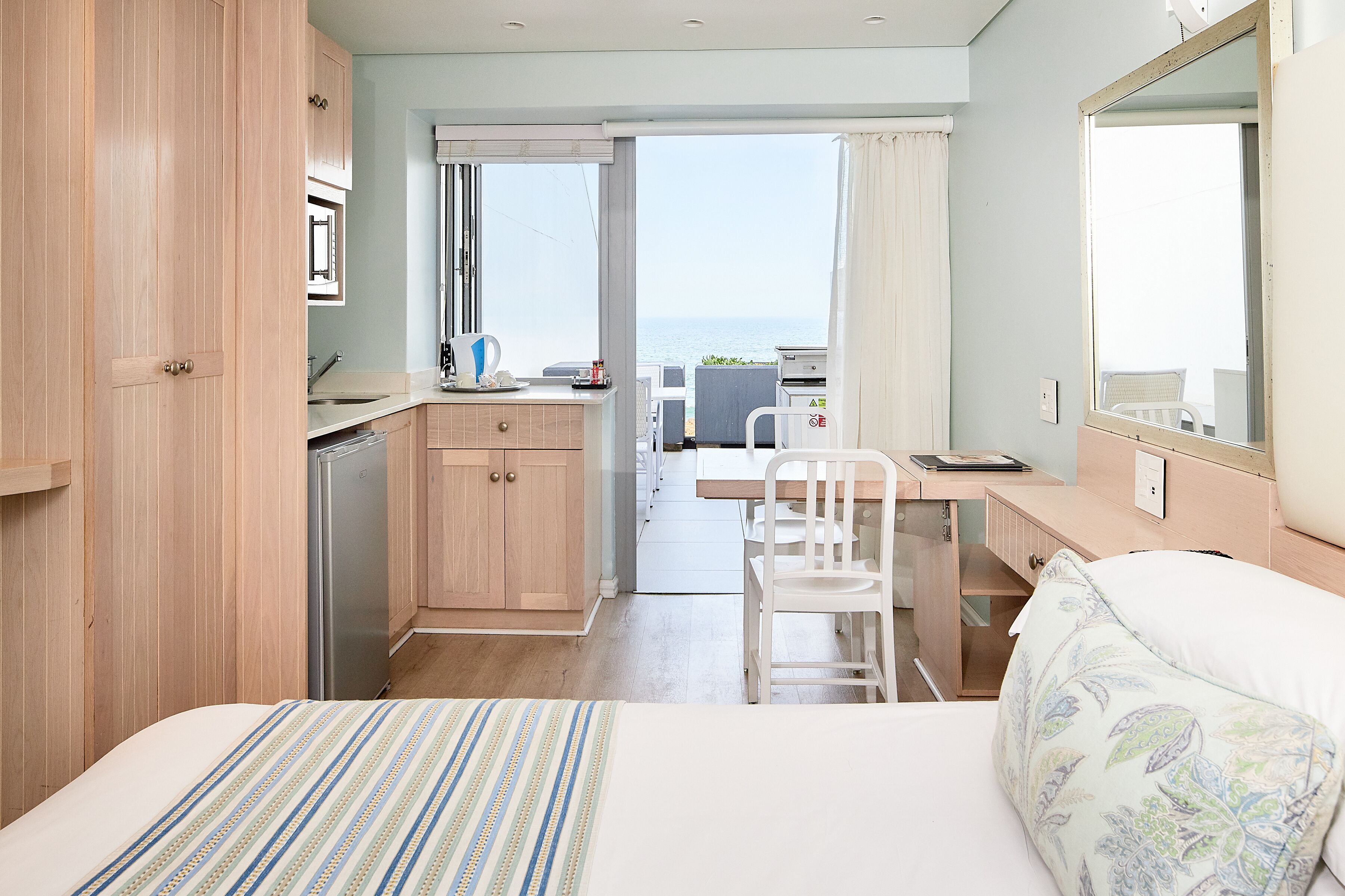 Un dormitorio con cama, escritorio, silla, kitchenette pequeño y vista al mar.