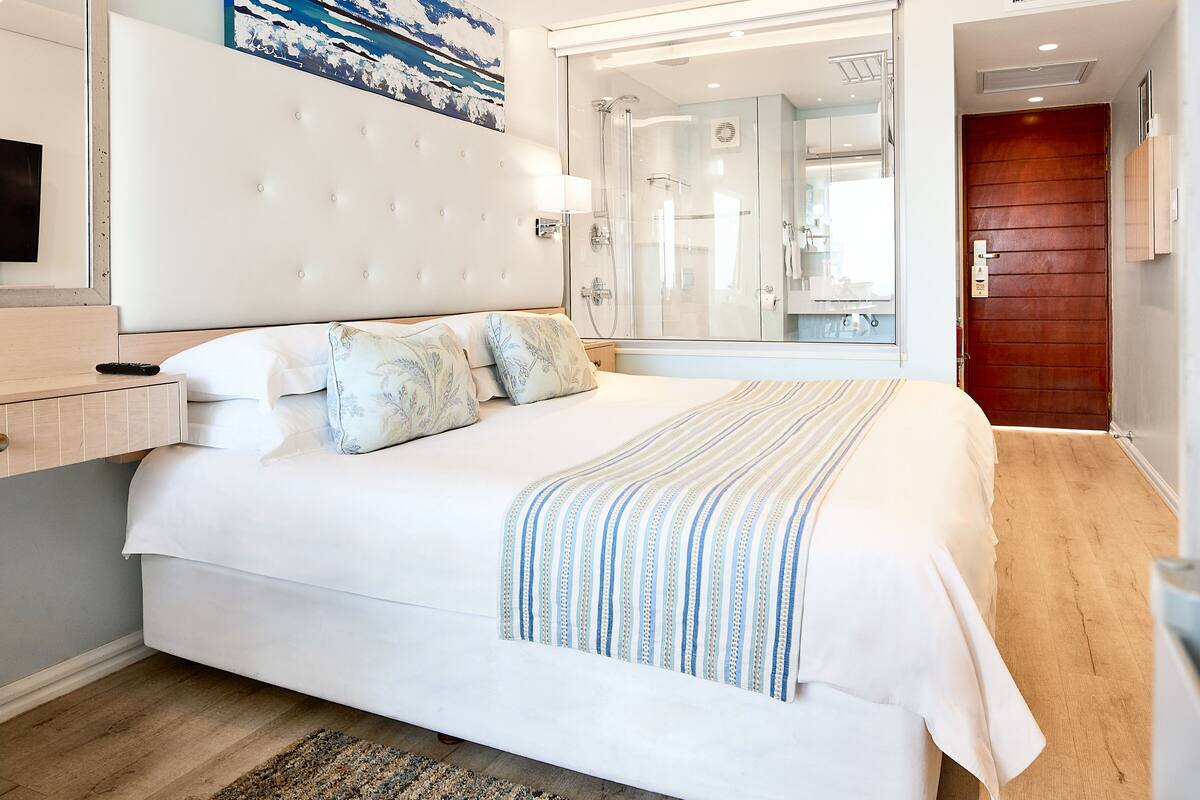 Habitación de hotel con una cama grande, televisor, baño con ducha y puerta de madera.