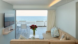 Uma sala de estar moderna com um sofá, uma mesa de centro com um vaso de rosas vermelhas, uma TV de tela plana e uma varanda com vista para o mar.