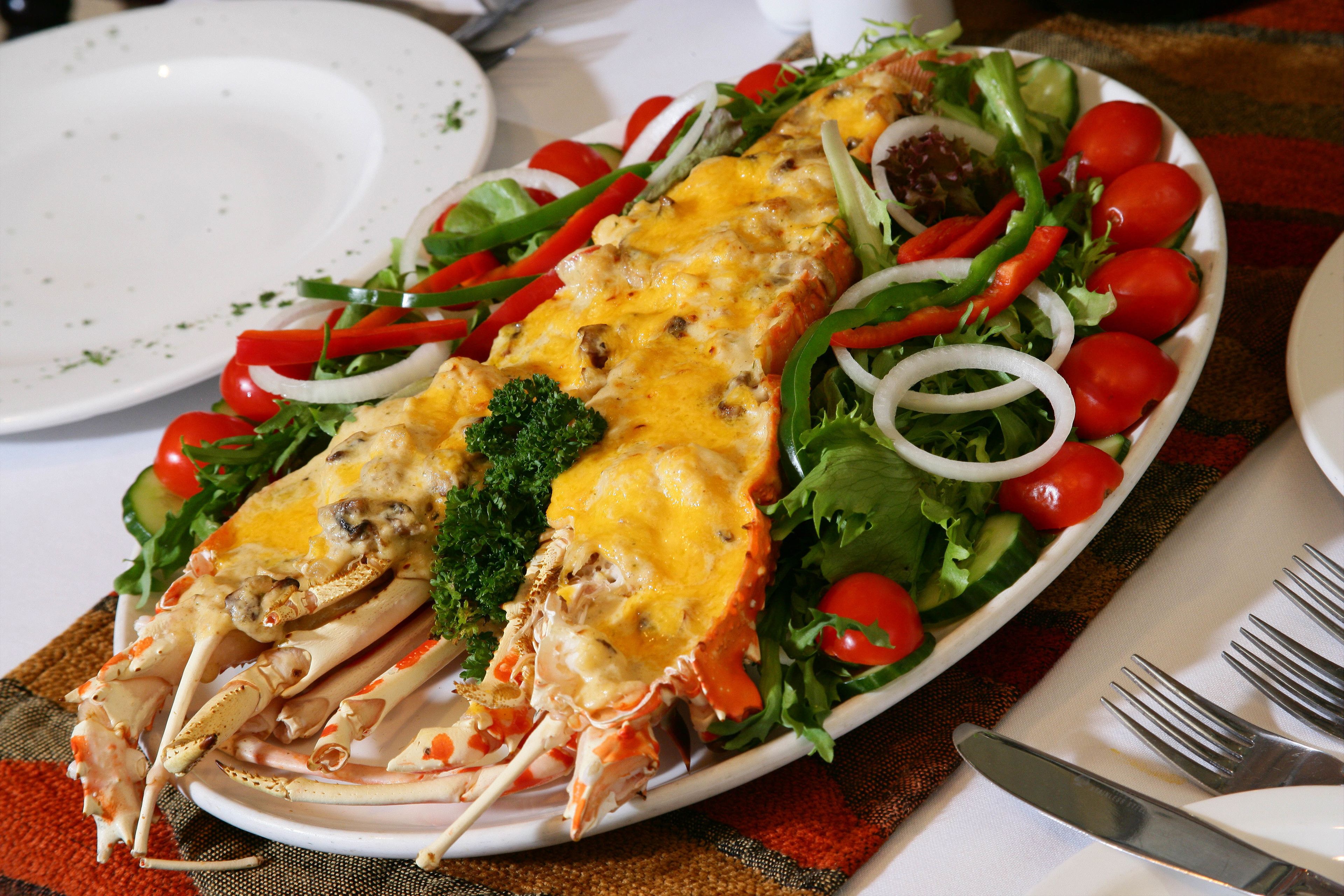 A seafood dish with a lobster tail, cheese, and vegetables on a plate.