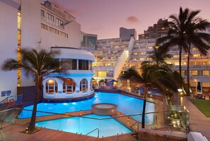Un hôtel doté d’une grande piscine, de palmiers et d’un bâtiment moderne avec des balcons.