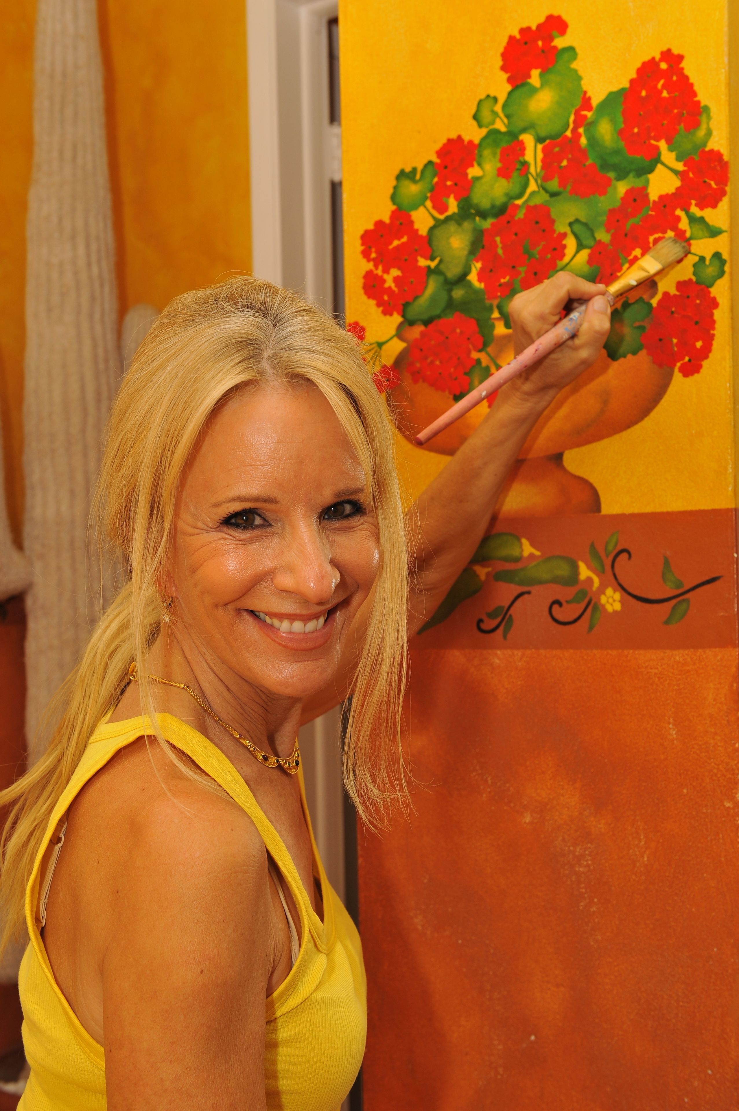 A person holding a paintbrush, painting a vibrant floral design on a wall.