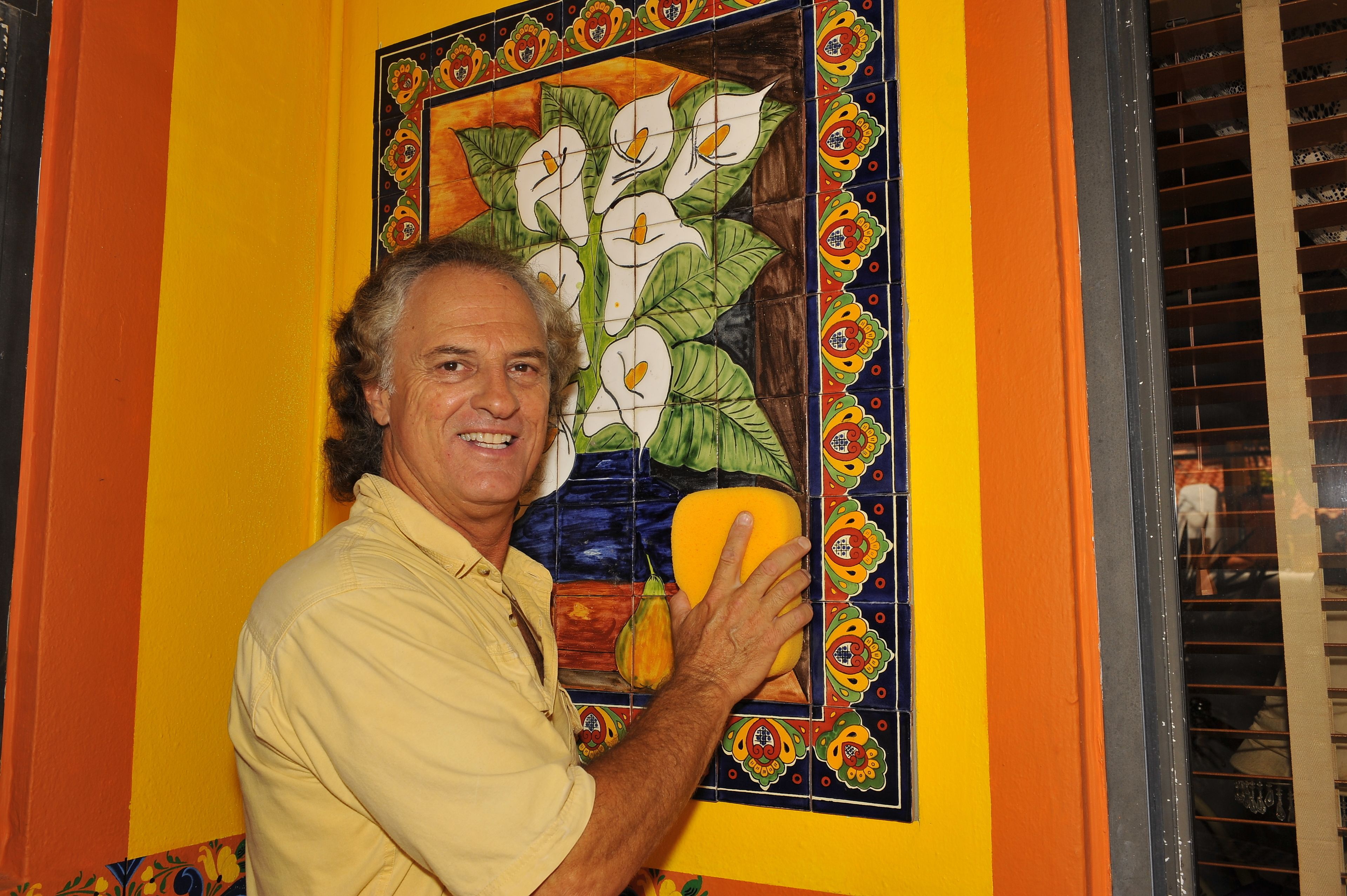 A man holding a yellow object in front of a colorful tiled wall with a floral pattern.
