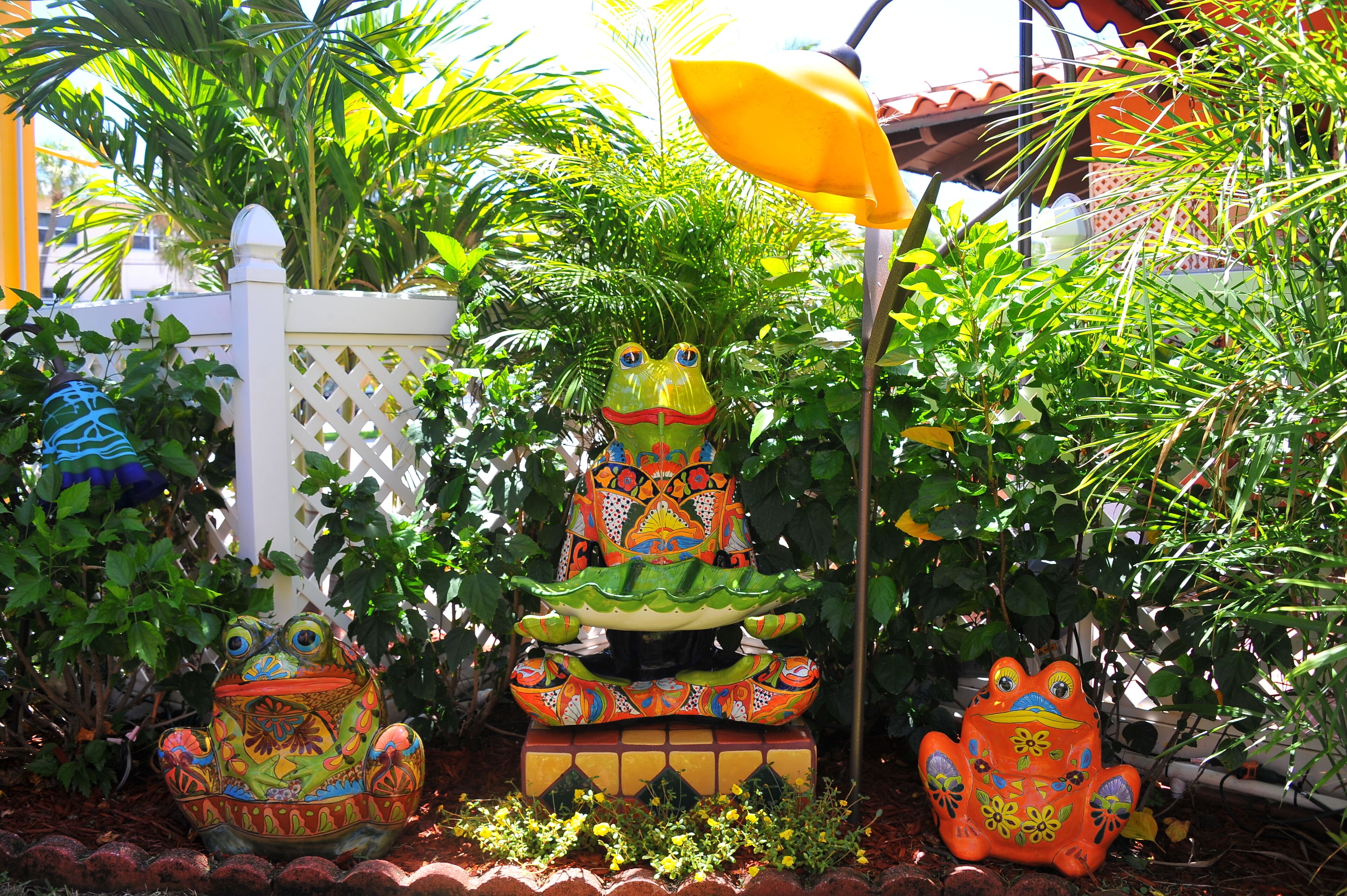 A garden with a decorative frog fountain and a white lattice fence.