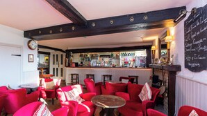 A cozy pub with red upholstered chairs, a bar area with various bottles, and a chalkboard menu.