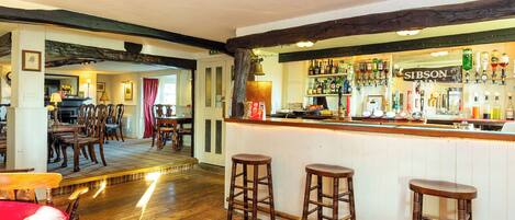 A bar area with wooden stools, a bar counter with various bottles, and a sign reading "SIBSON".