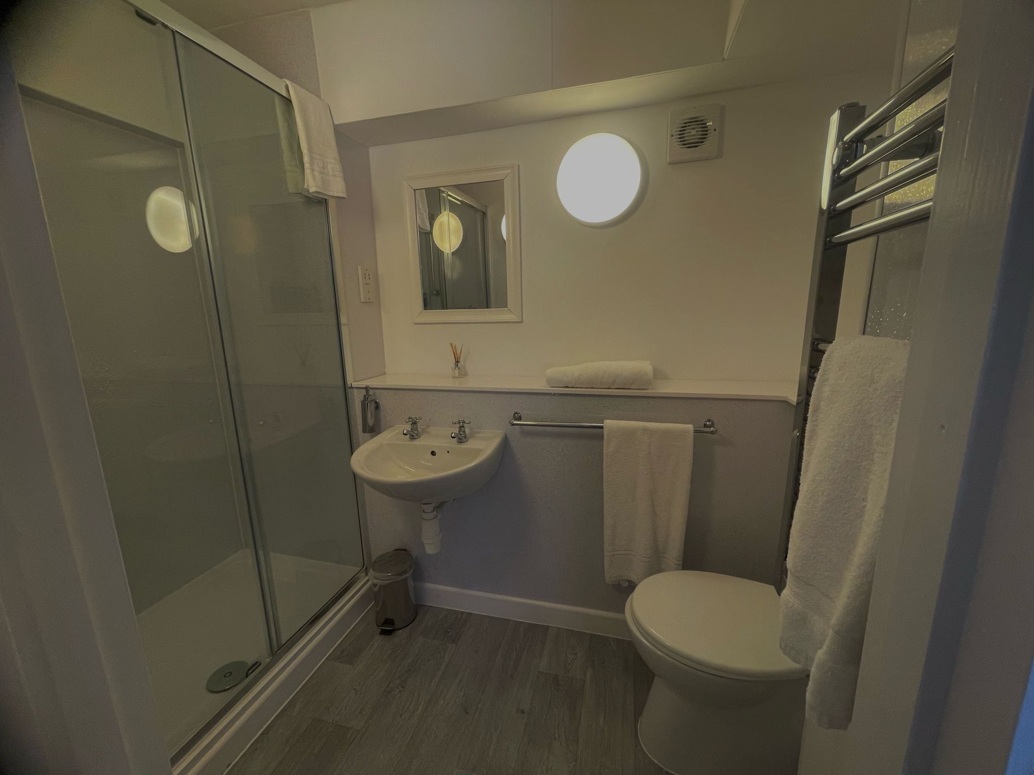 Een badkamer met een douchecabine van glas, een wastafel, toilet en een handdoekhouder.