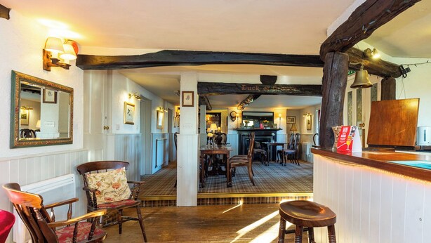 A traditional inn with a wooden floor, a bar area, and a dining space with wooden furniture.