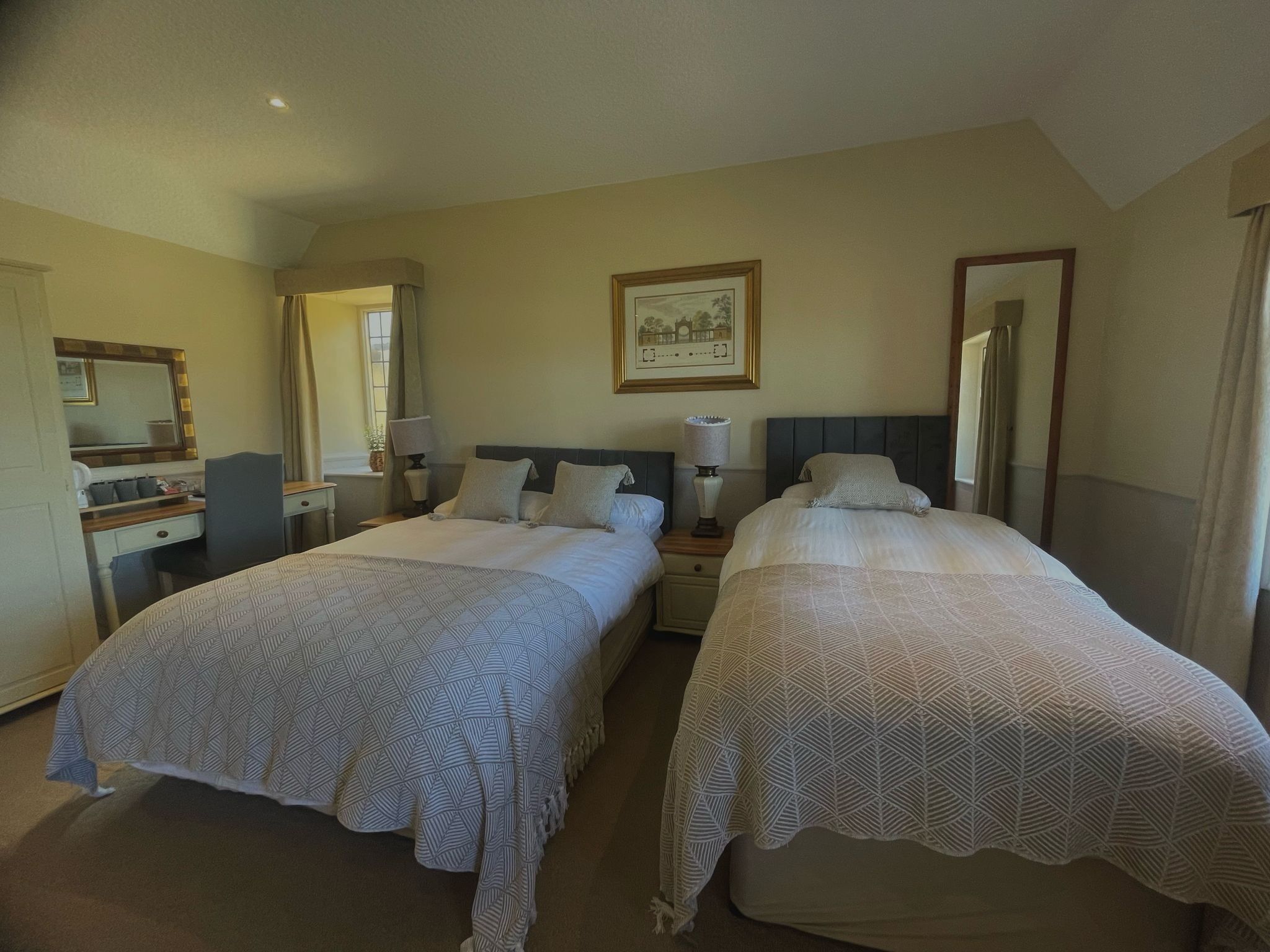A hotel room with two beds, a desk, a chair, a mirror, and a framed picture on the wall.
