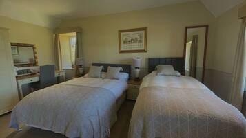 A hotel room with two beds, a desk, a chair, a mirror, and a framed picture on the wall.