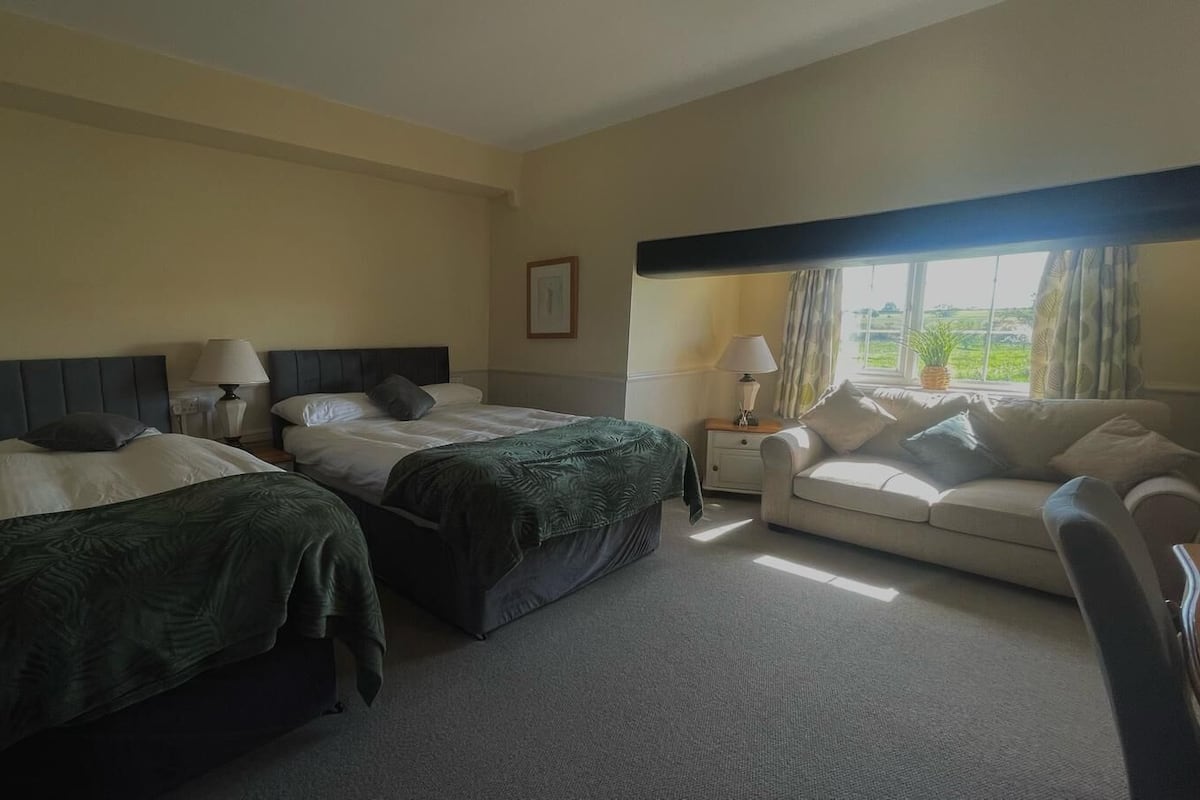 Une chambre d’hôtel avec deux lits simples, un canapé, une petite table et une fenêtre avec des rideaux.