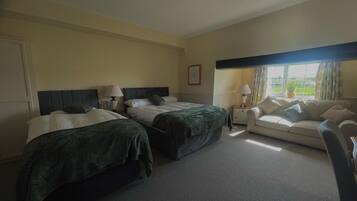 Habitación de hotel con dos camas individuales, un sofá, una mesita y una ventana con cortinas.