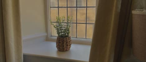 A window with a potted plant on a white sill, curtains partially drawn, and a wooden table in the foreground.