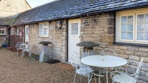 A stone building with numbered doors, outdoor seating, and a gravel ground.