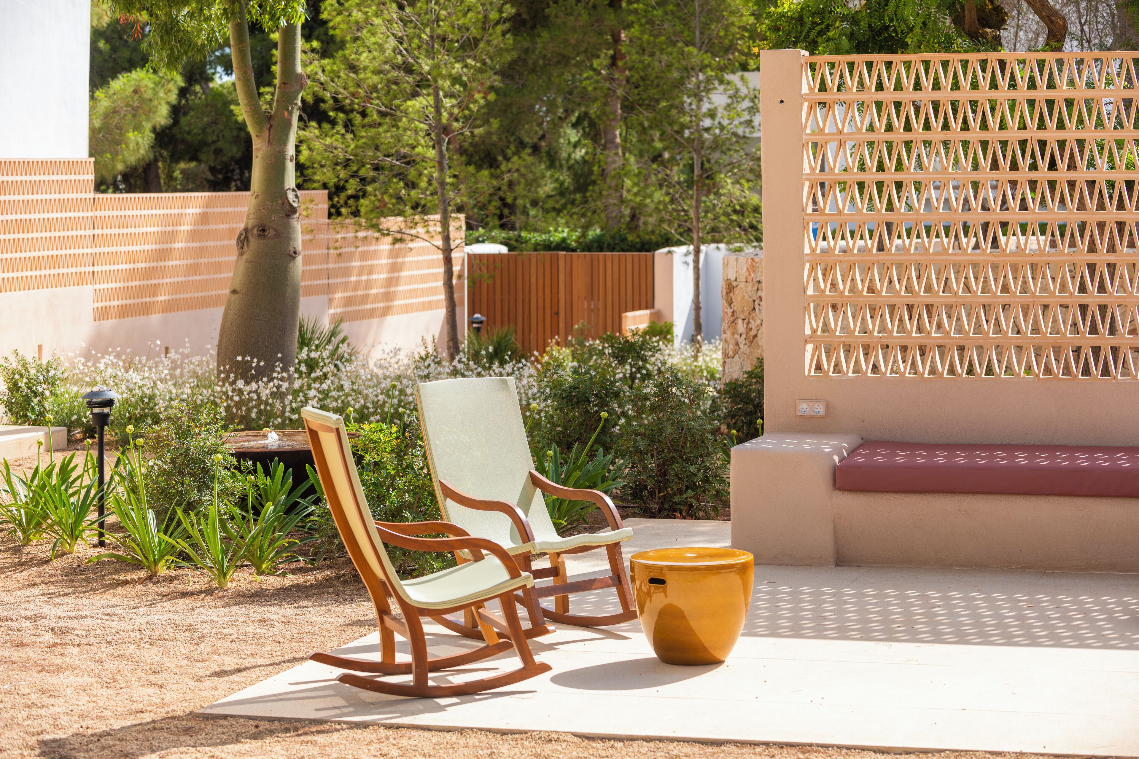 A patio area with two rocking chairs, a yellow pot, and a beige bench.