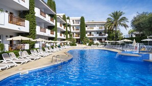 A swimming pool with lounge chairs and umbrellas, surrounded by multi-story buildings with balconies. - Inturotel Esmeralda Garden (Santanyi)