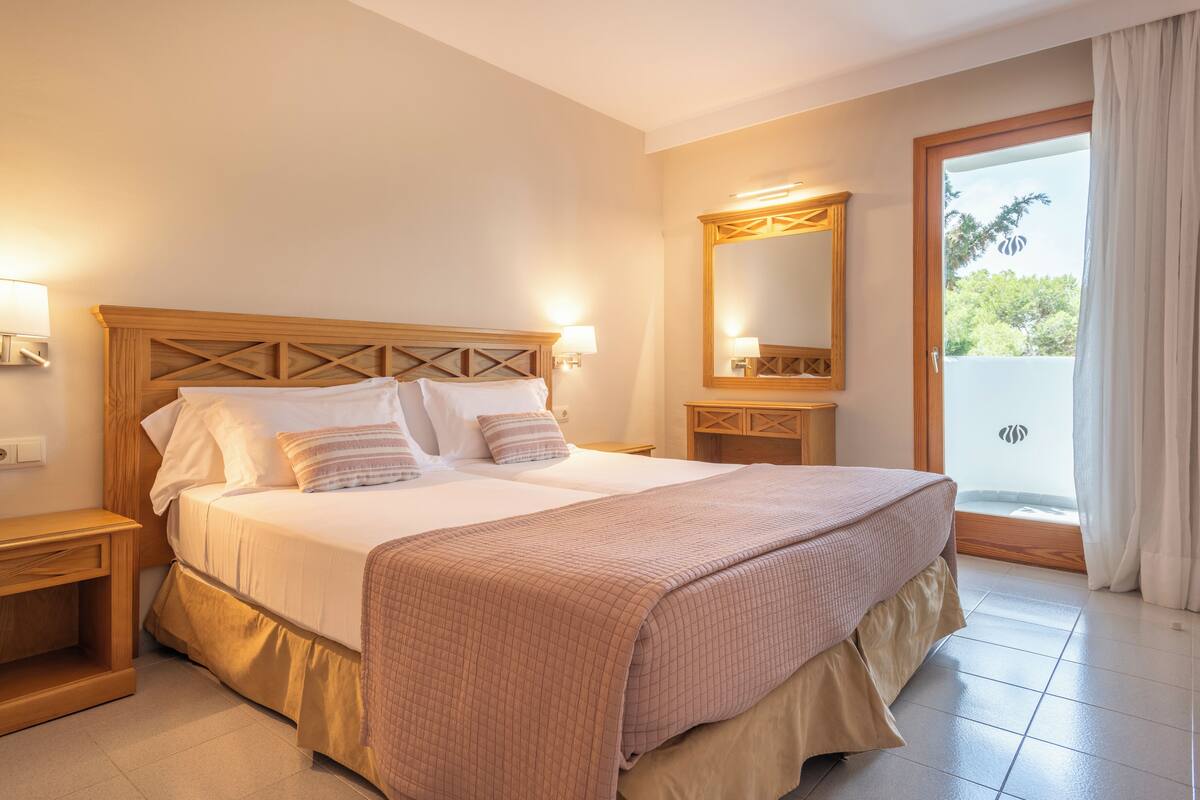 Un letto matrimoniale con testiera in legno, due comodini, un grande specchio e vista all'esterno tramite una porta scorrevole in vetro.