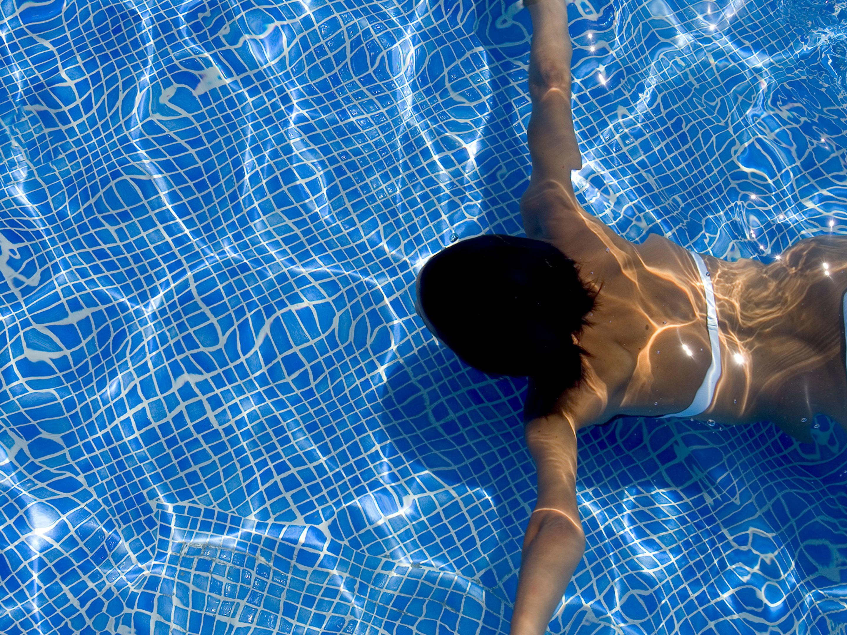 Una persona nadando en una piscina con un llamativo diseño de mosaico azul.