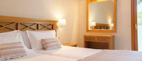 A double bed with two pillows, a bedside table, a mirror, and a wooden headboard.